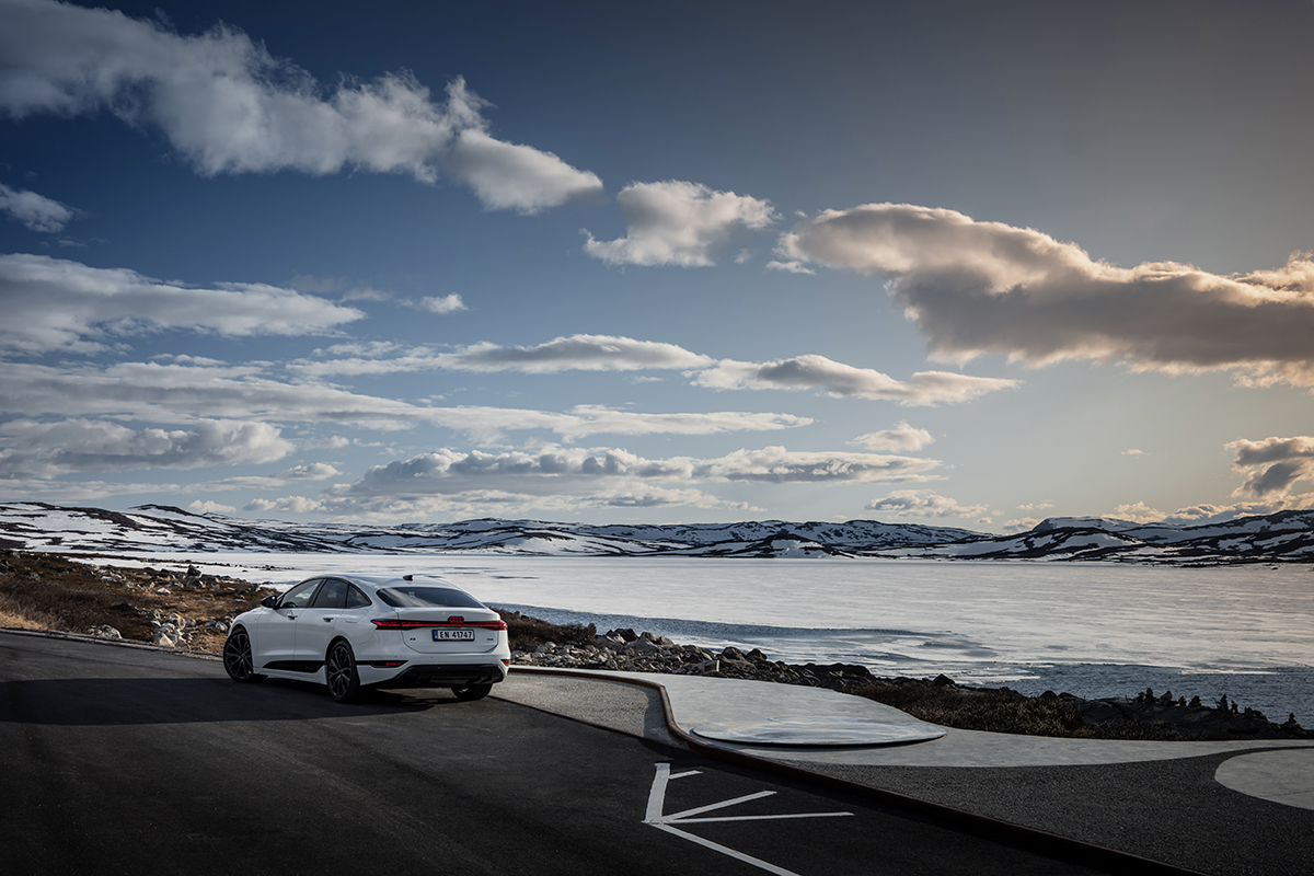 Audi A6 Sportback e-tron performance v beli barvi stoji na parkirišču tik ob zamrznjenem jezeru na Norveškem. 