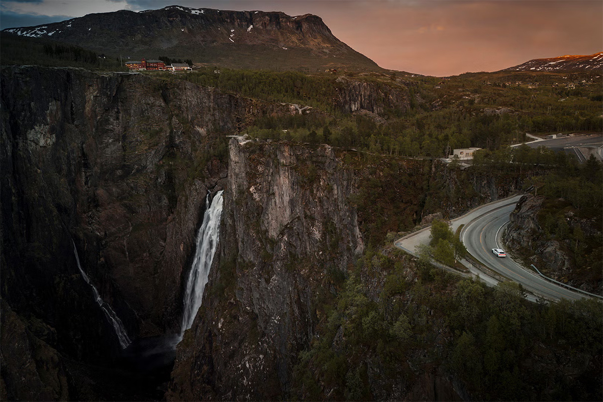 Audi A6 Sportback e-tron performance na ovinkasti cesti z razgledom na gorovje in slap Vøringsfossen.