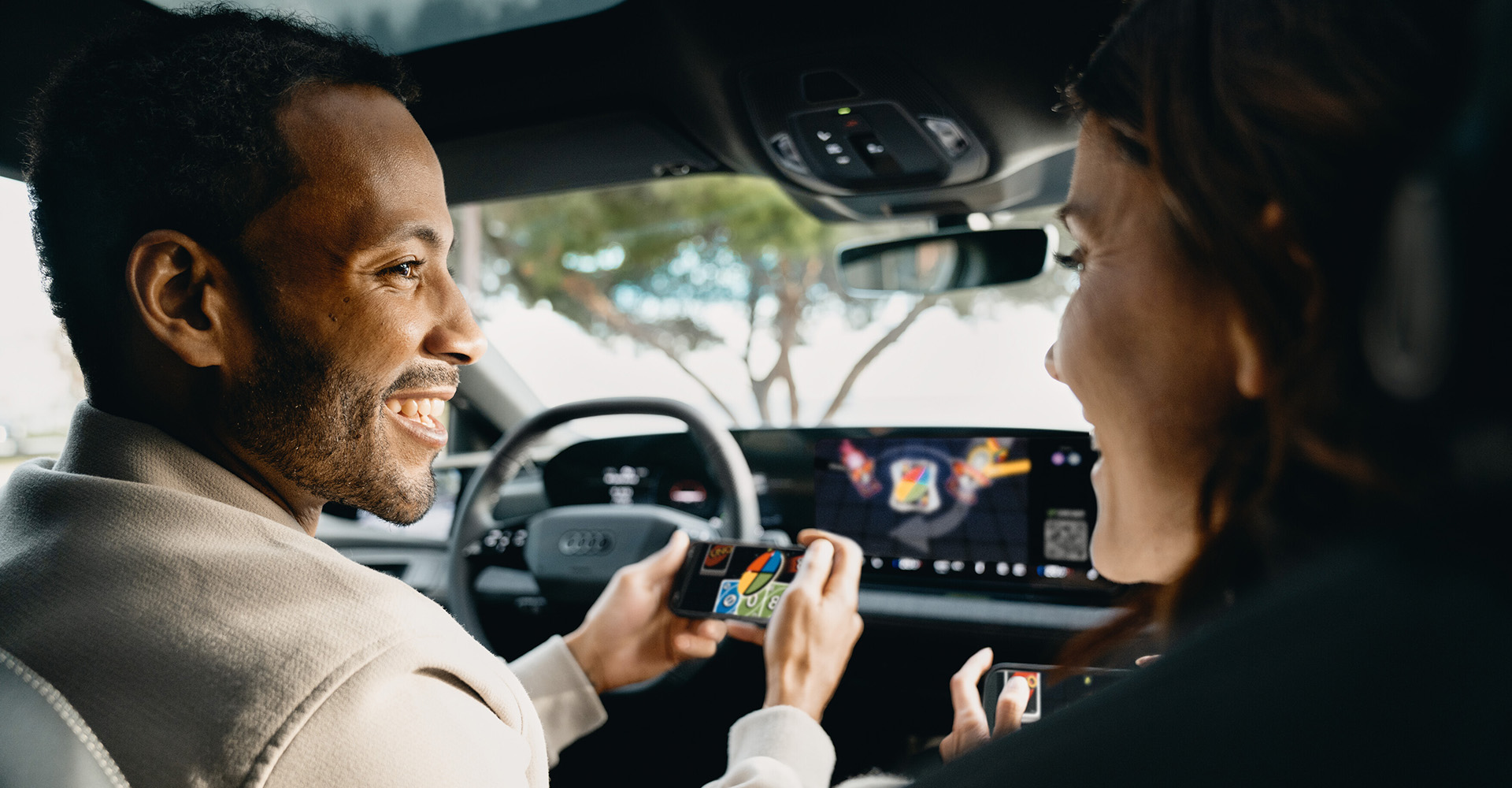 Igrica AirConsole teče na zaslonu v Audiju; voznik in sopotnik se igrata s telefoni kot krmilniki.