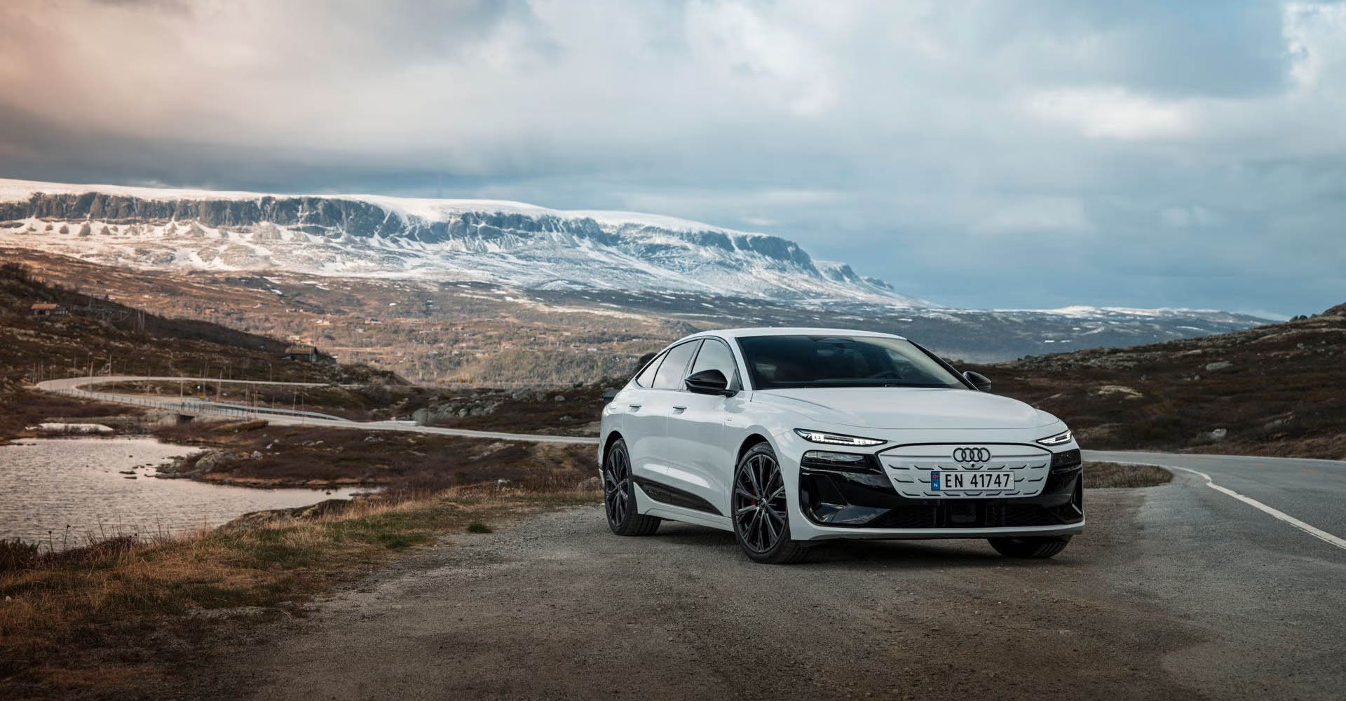 Bel Audi A6 Sportback e-tron pred skandinavsko pokrajino z gorami in gozdovi.
