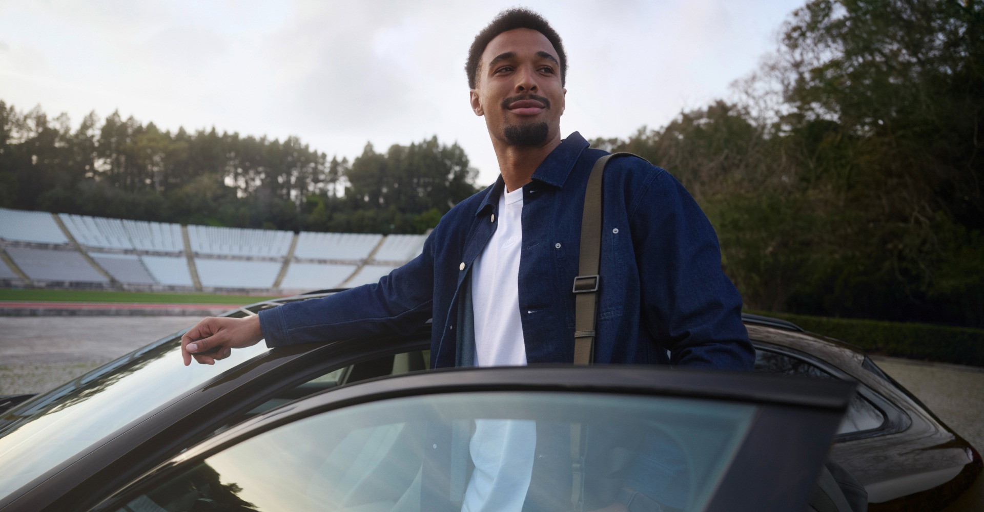Leo Neugebauer stoji med odprtimi voznikovimi vrati modela Audi A6 Avant, parkiranega na stadionu.