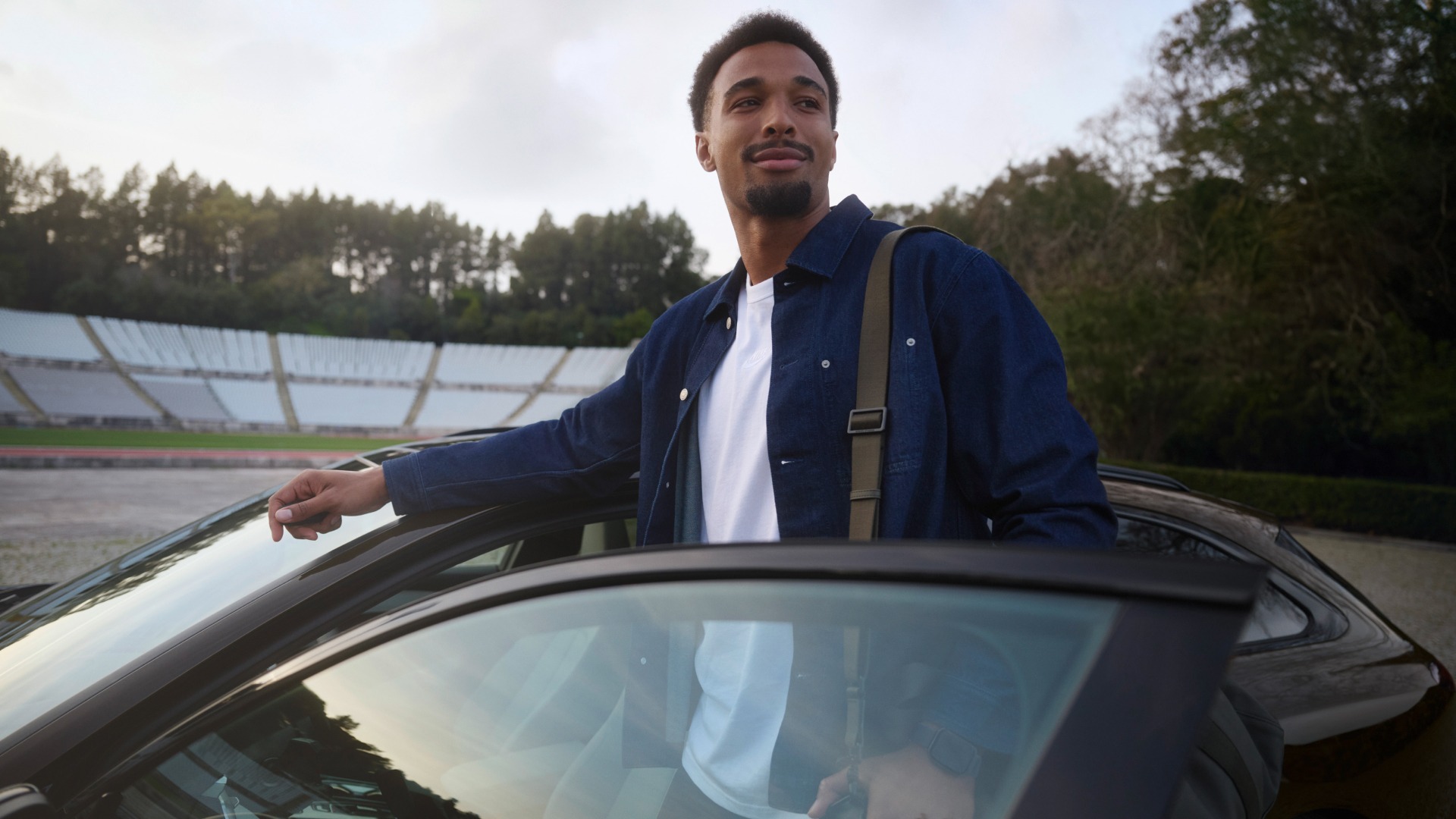 Leo Neugebauer stoji med odprtimi voznikovimi vrati modela Audi A6 Avant, parkiranega na stadionu.