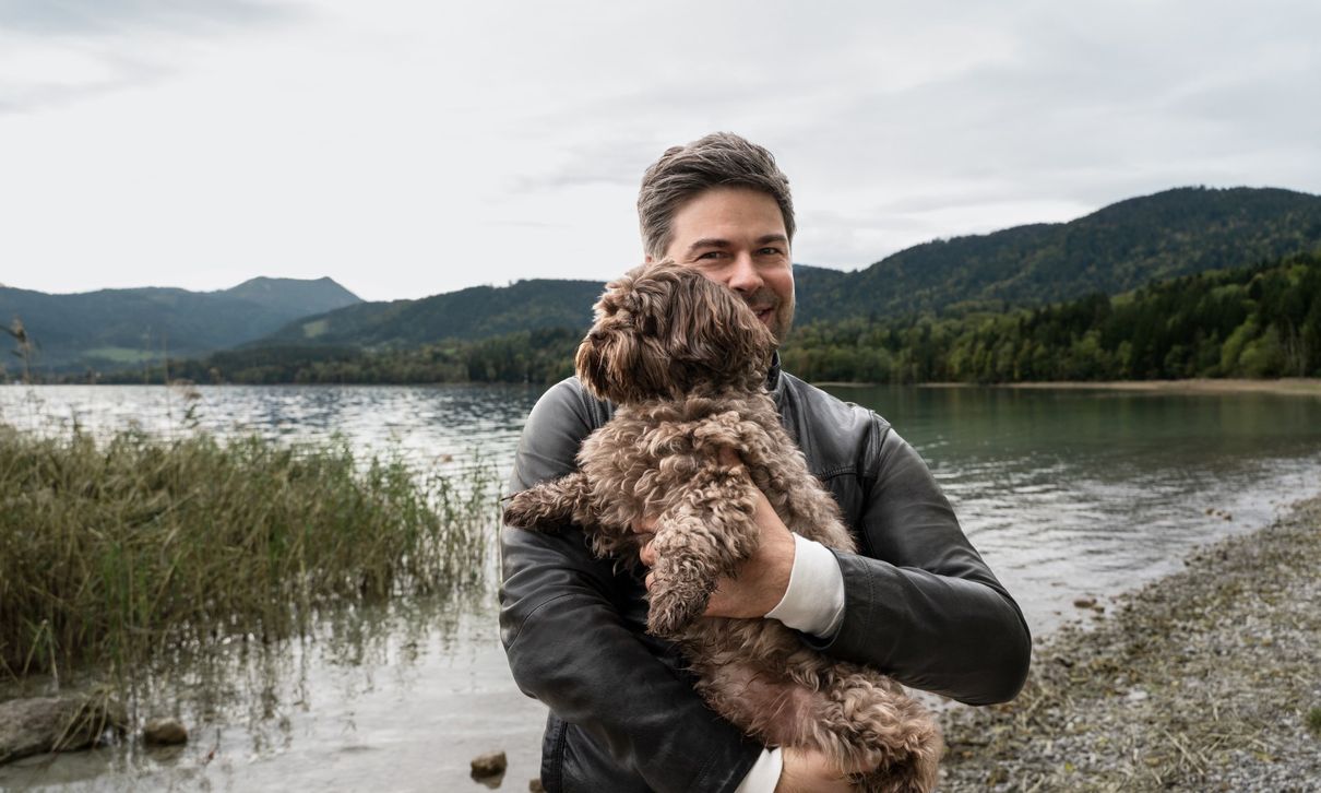 Nils Wollny stoji ob jezeru s psom v naročju.