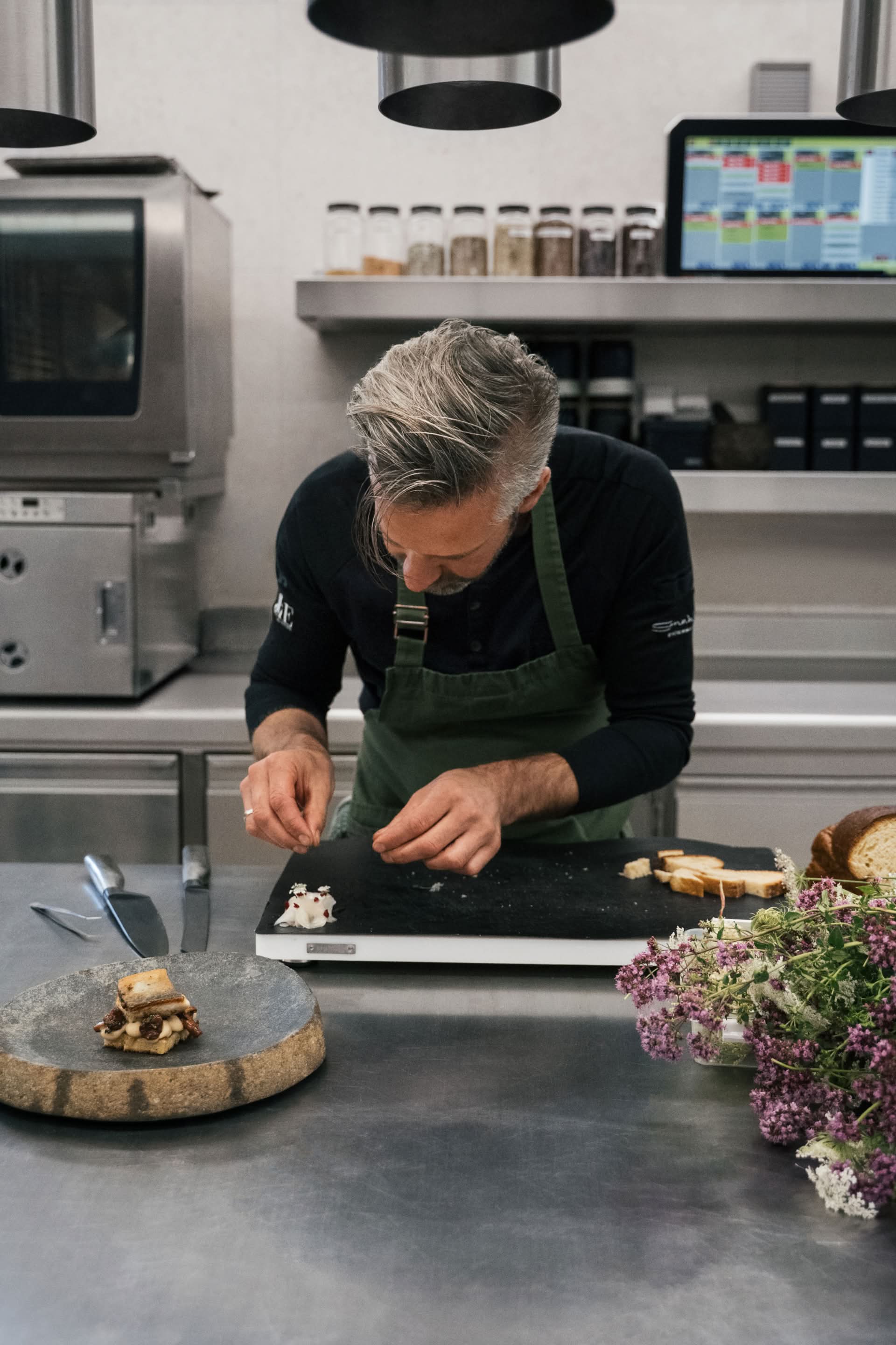 Vitus Winkler pripravlja jed v kuhinji, v ospredju so zelišča.