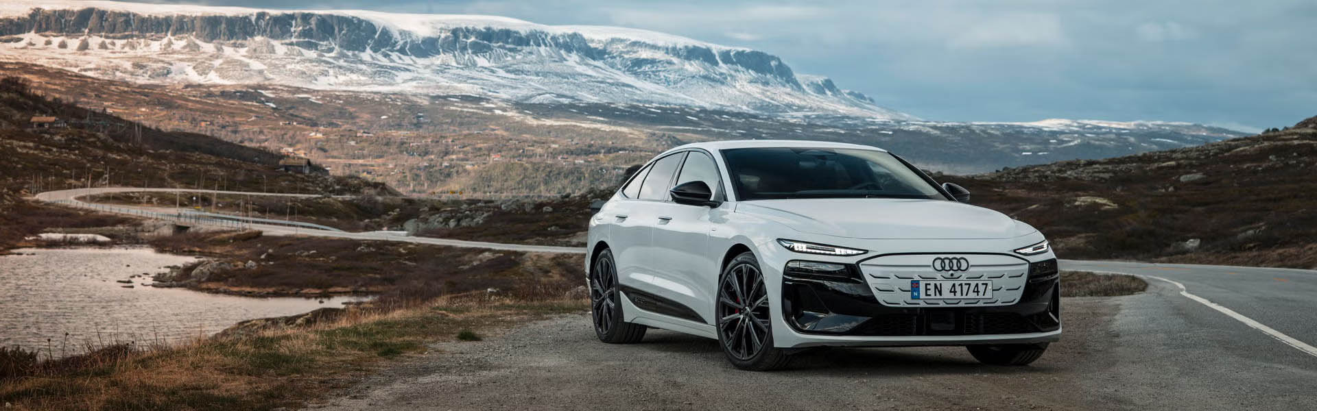 Bel Audi A6 Sportback e-tron pred skandinavsko pokrajino z gorami in gozdovi.