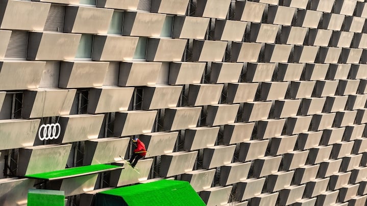 Smučar med skokom na zeleni umetni progi pred veliko fasado z Audi znakom