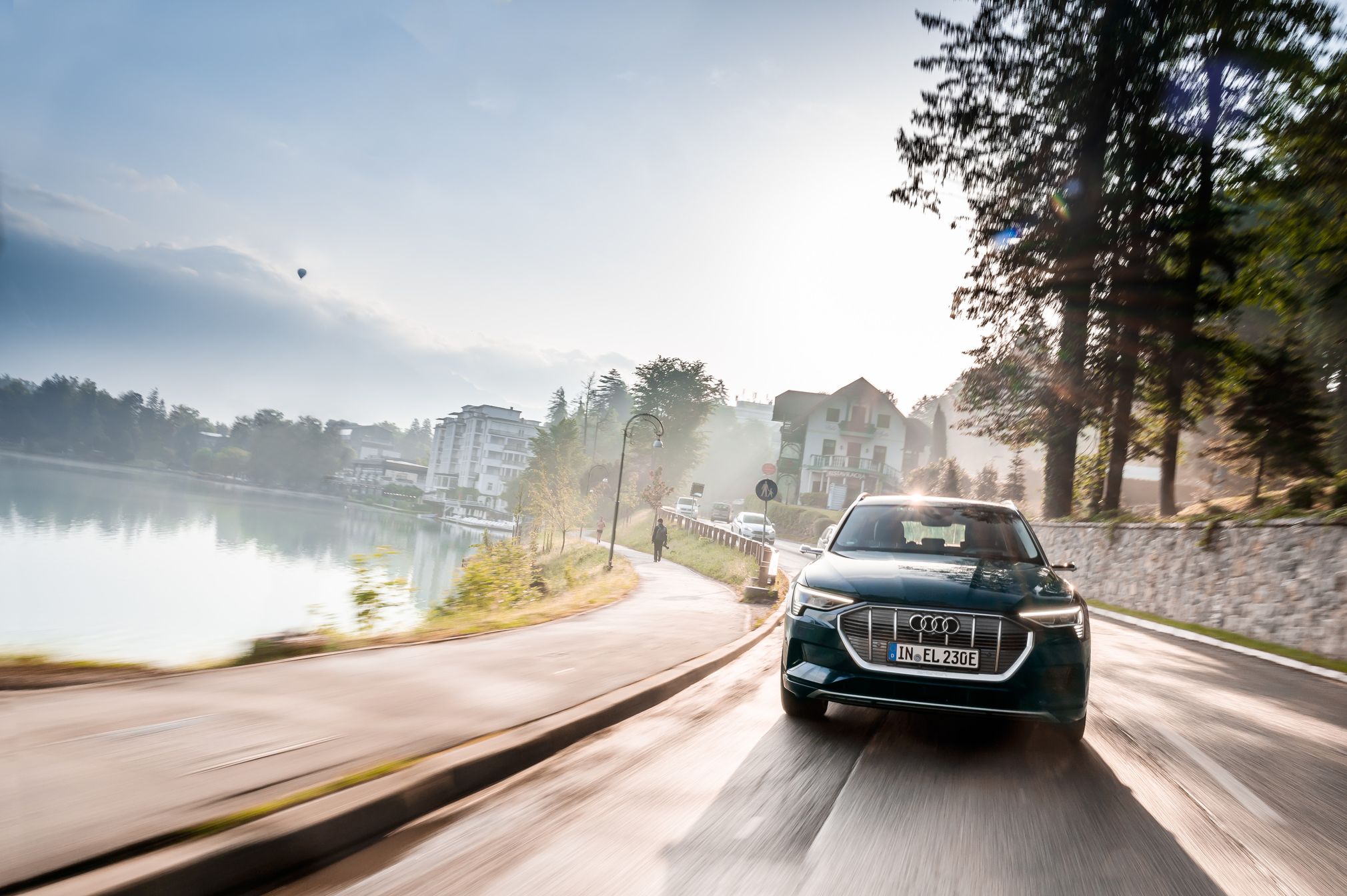 Audi e-tron na cesti ob Blejskem jezeru. V ozadju drugi avtomobili in hiše