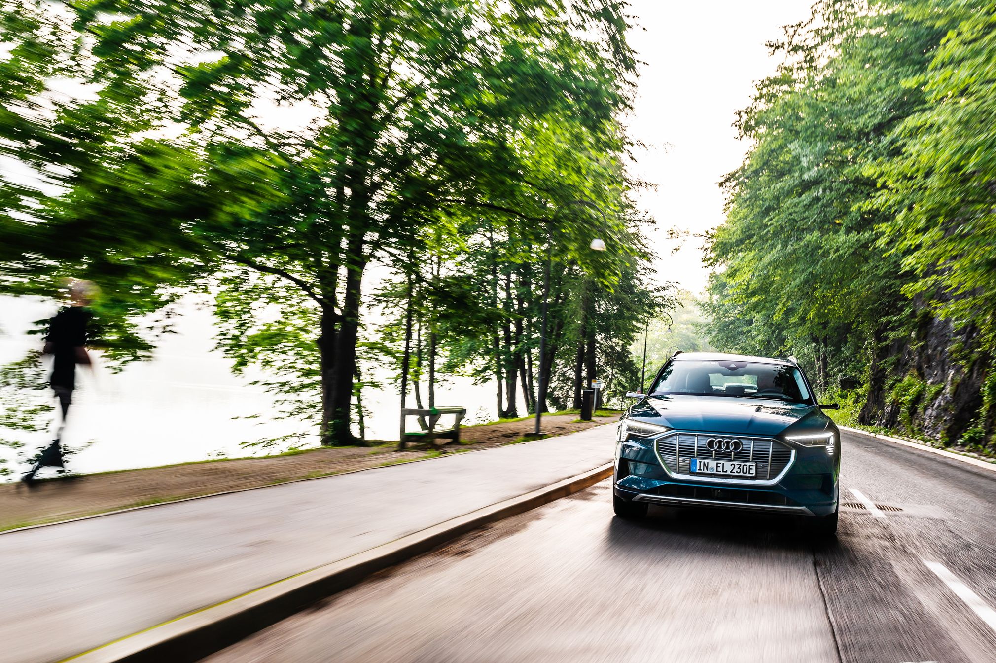Audi e-tron med vožnjo na cesti, ob cesti veliko zelenih dreves