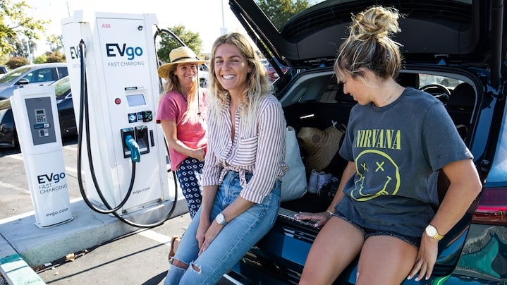 Tri ženske na bencinski postaji, se naslanjajo na prtljažnik Audi e-trona