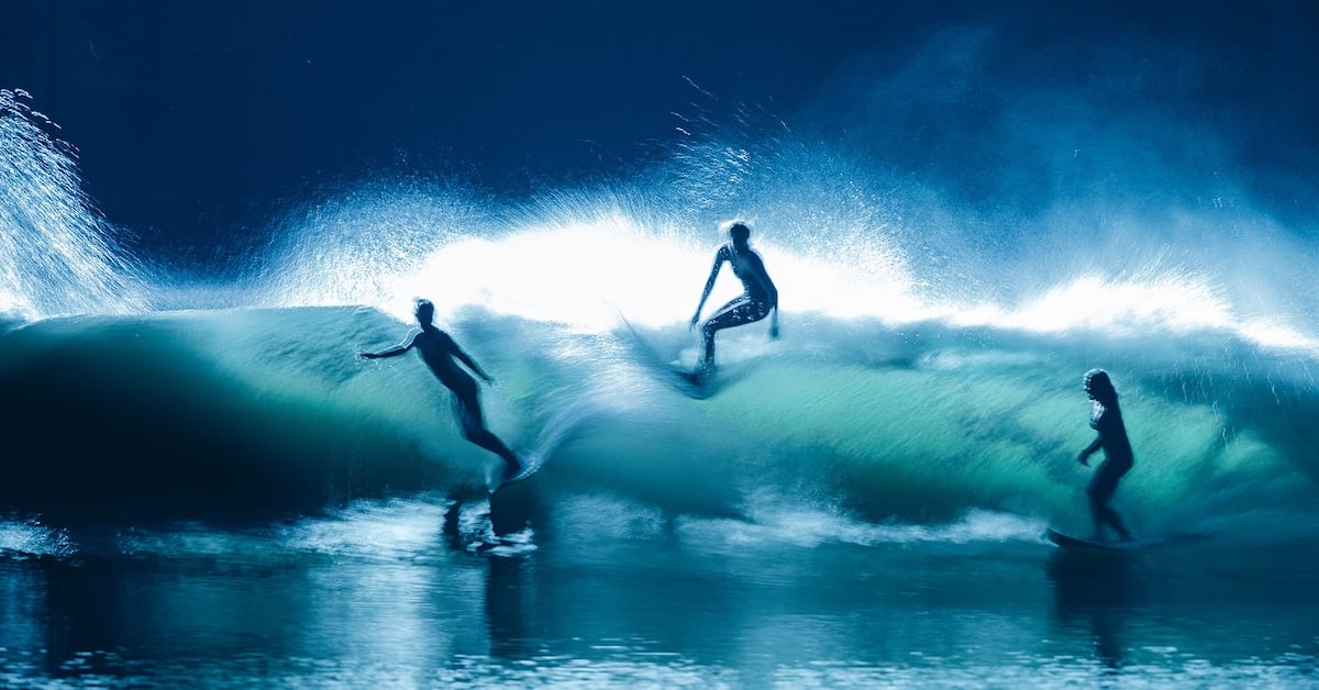 Tri ženske surferke na valovih. Ponoči, voda je temno modra