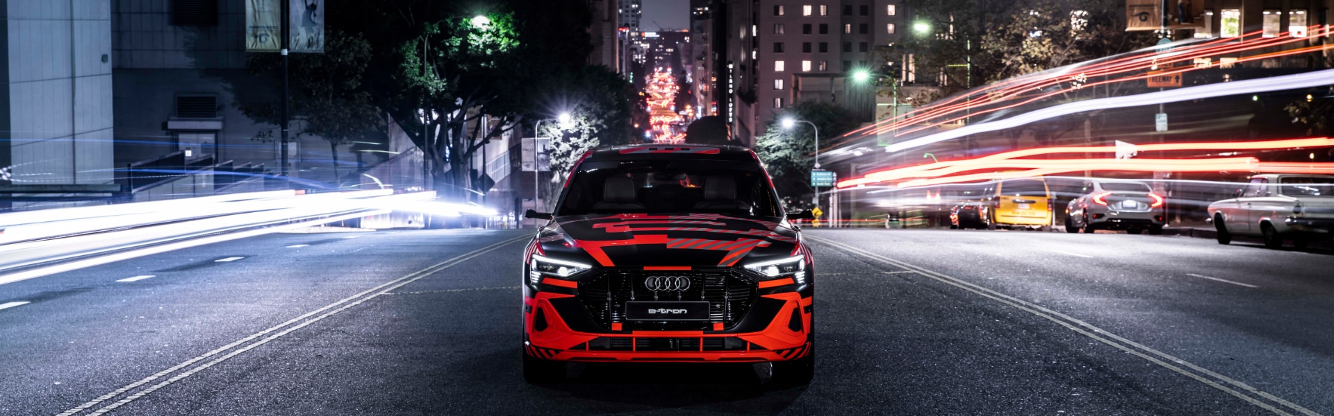 Rdeče vozilo Audi e-tron na cesti v mestu ponoči. Slikano od spredaj