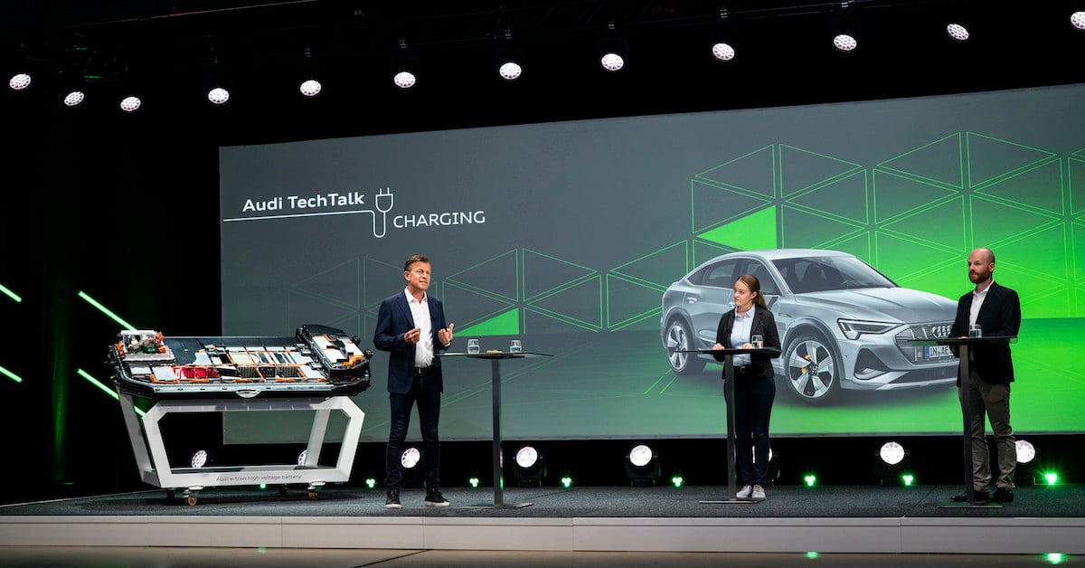 Trije predavatelji Audi Tech Talk na odru. V ozadju predstavitev, na sliki Audi e-tron sportback