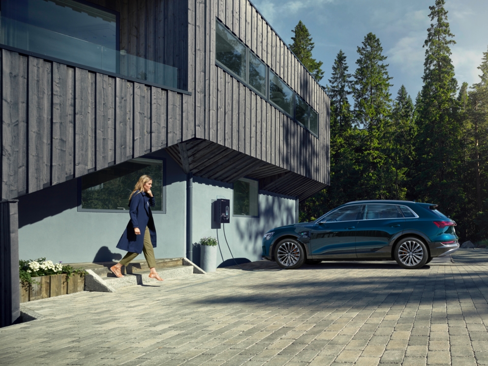 Moder Audi e-tron med polnjenjem pred sodobno hišo