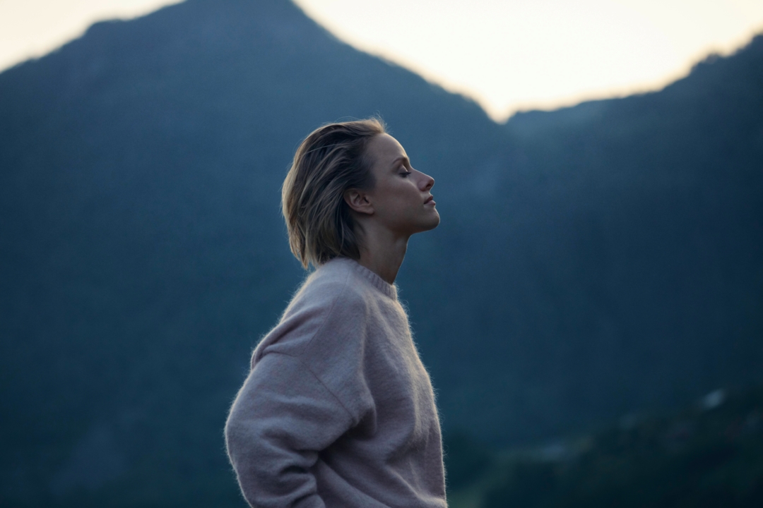 Ženska v puloverju, v ozadju gora in sončni zahod