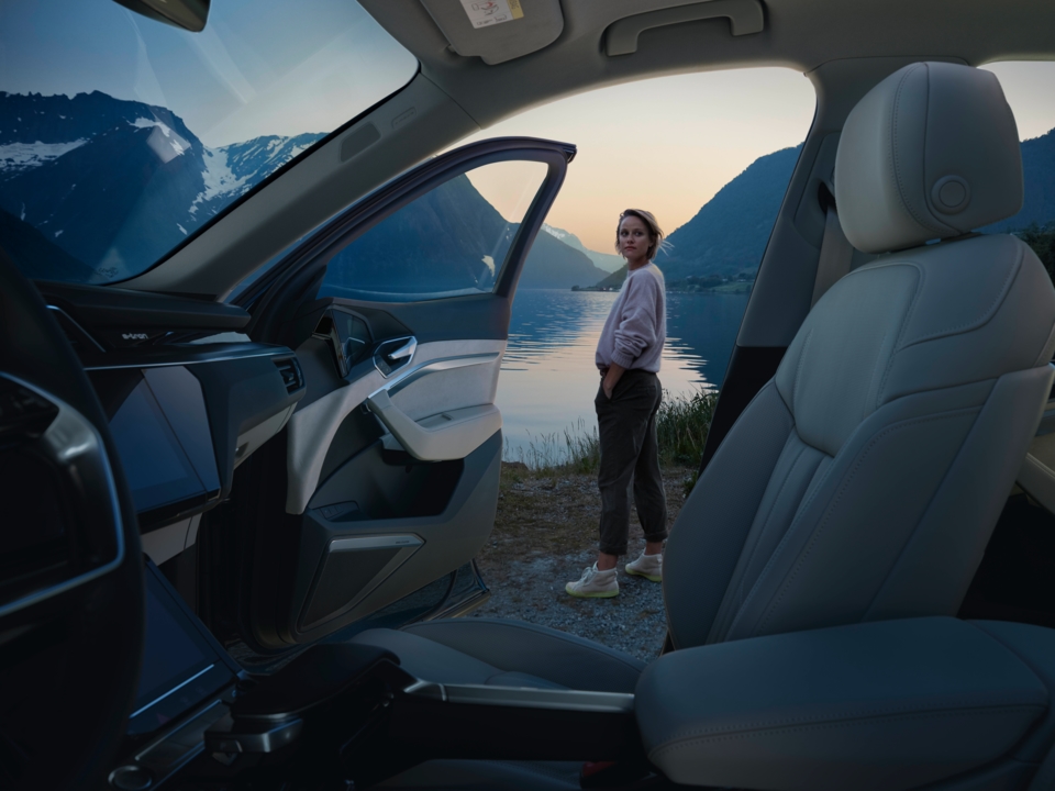 Notranjost Audi e-tron, v ozadju ženska, ki stoji pred jezerom. Ob sončnem zahodu