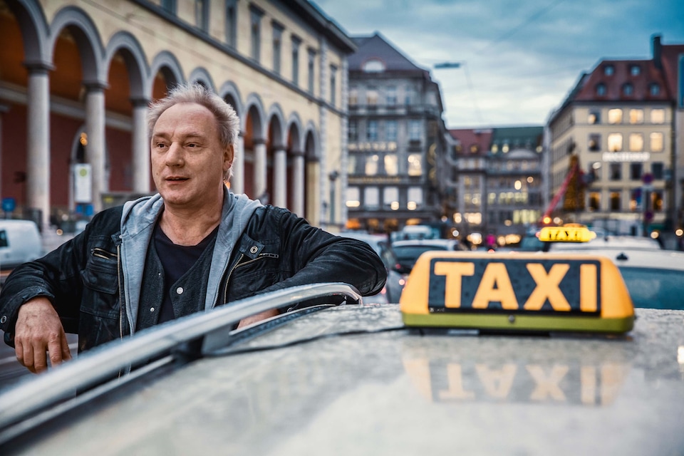 Taxist Franz, naslonjen na svoj rumen taxi avtomobil