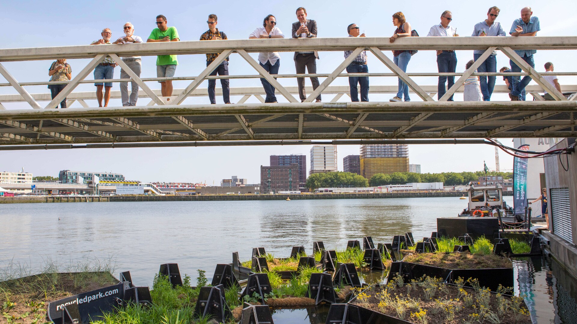 ljudje z mostu opazujejo plastične otoke na reki  Nieuwe Maas