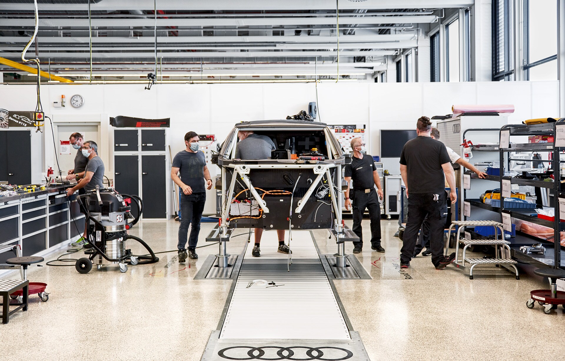 Zaposleni v Audi Sport delajo na dvignjeni kletki dirkalnika v delavnici. 
