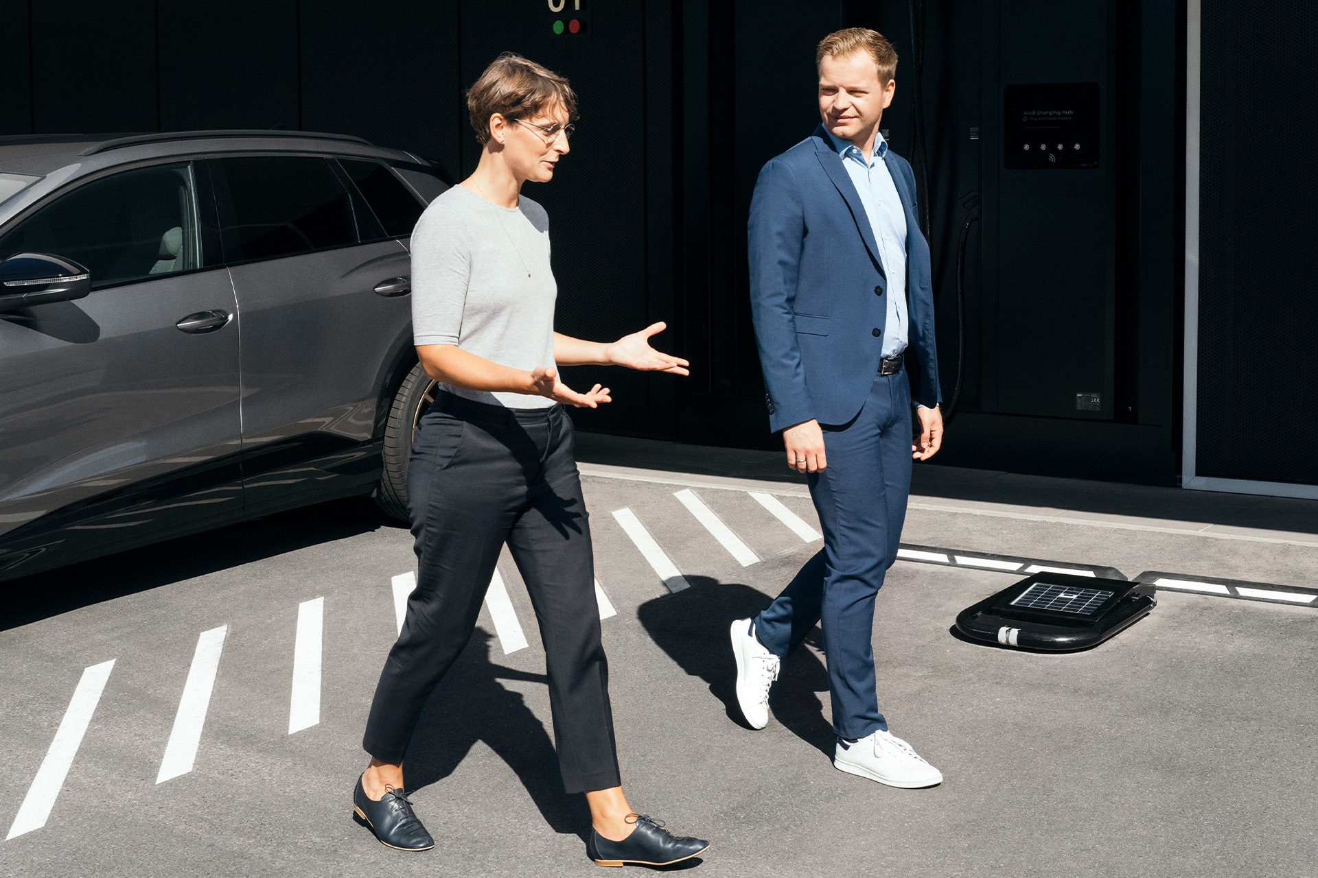 Strokovnjaka za trajnostni razvoj dr. Johanna Klewitz in Malte Vömel se sprehajata po parkirišču pred polnilnim središčem Audi charging hub v Nürnbergu.