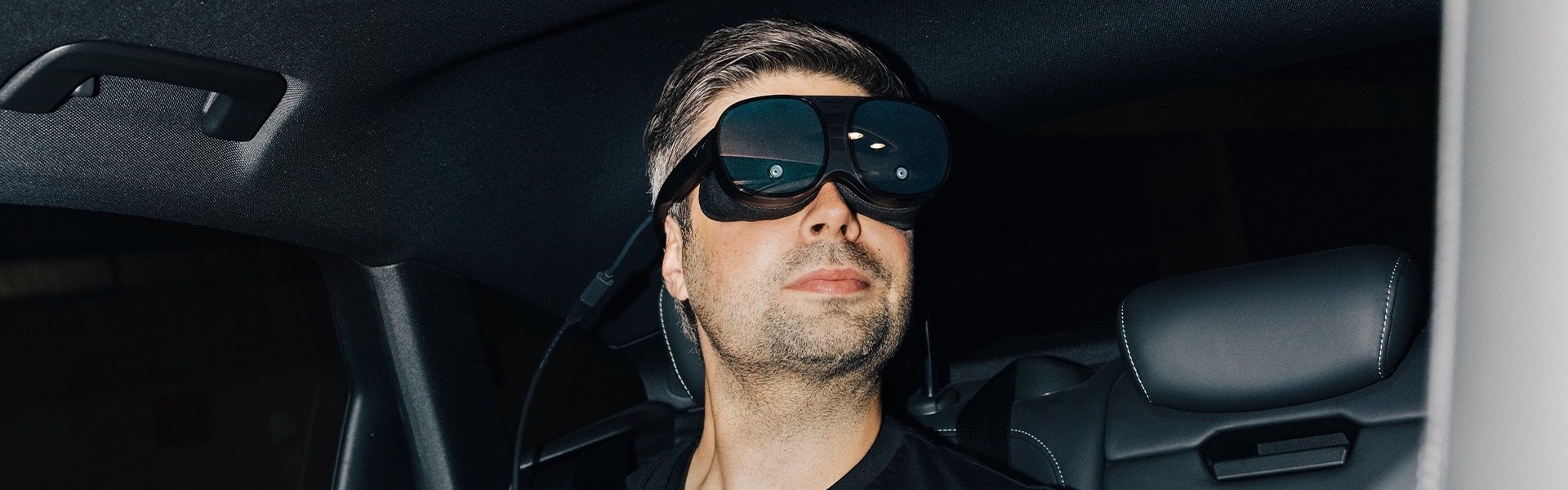Nils Wollny sedi na zadnjem sedežu vozila Audi in nosi očala za navidezno resničnost.