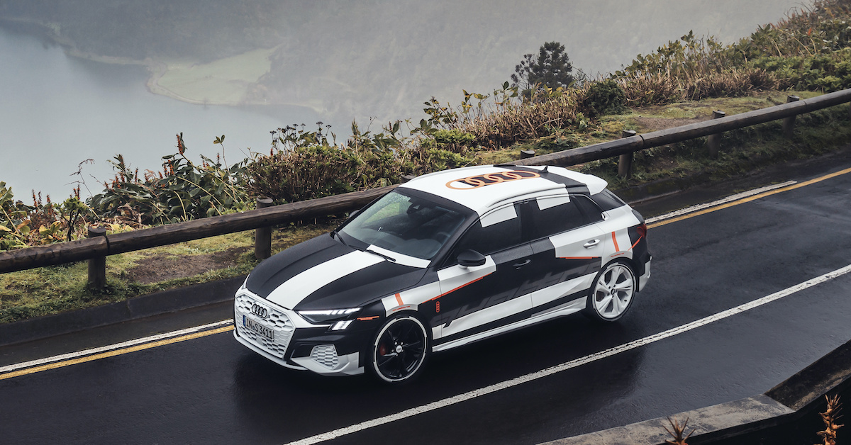 Prototip vozilo Audi na gorski cesti pred vstopom v tunel. V ozadju jezero in oblačno nebo