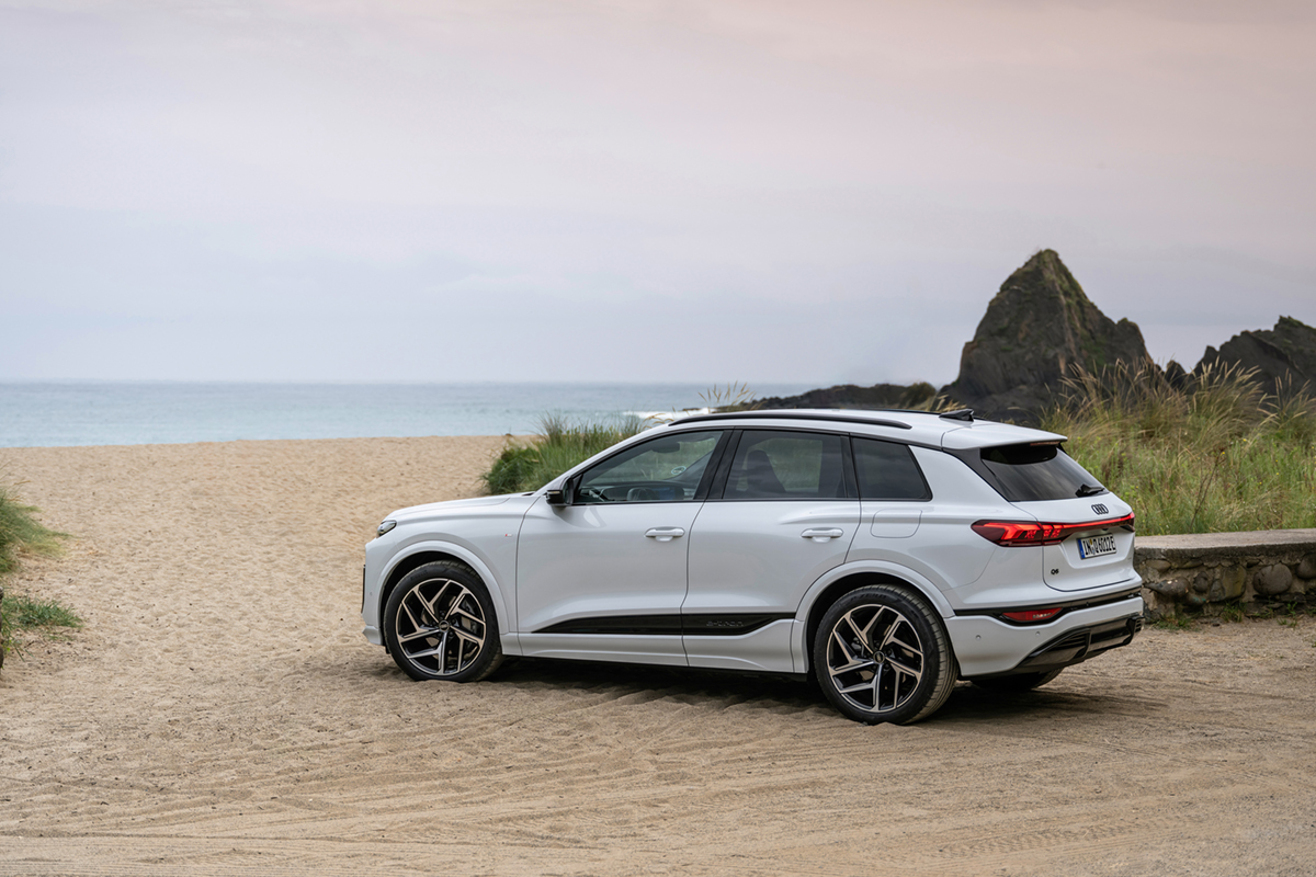 Bel Audi Q6 SUV e-tron na široki peščeni plaži, v ozadju je morje.