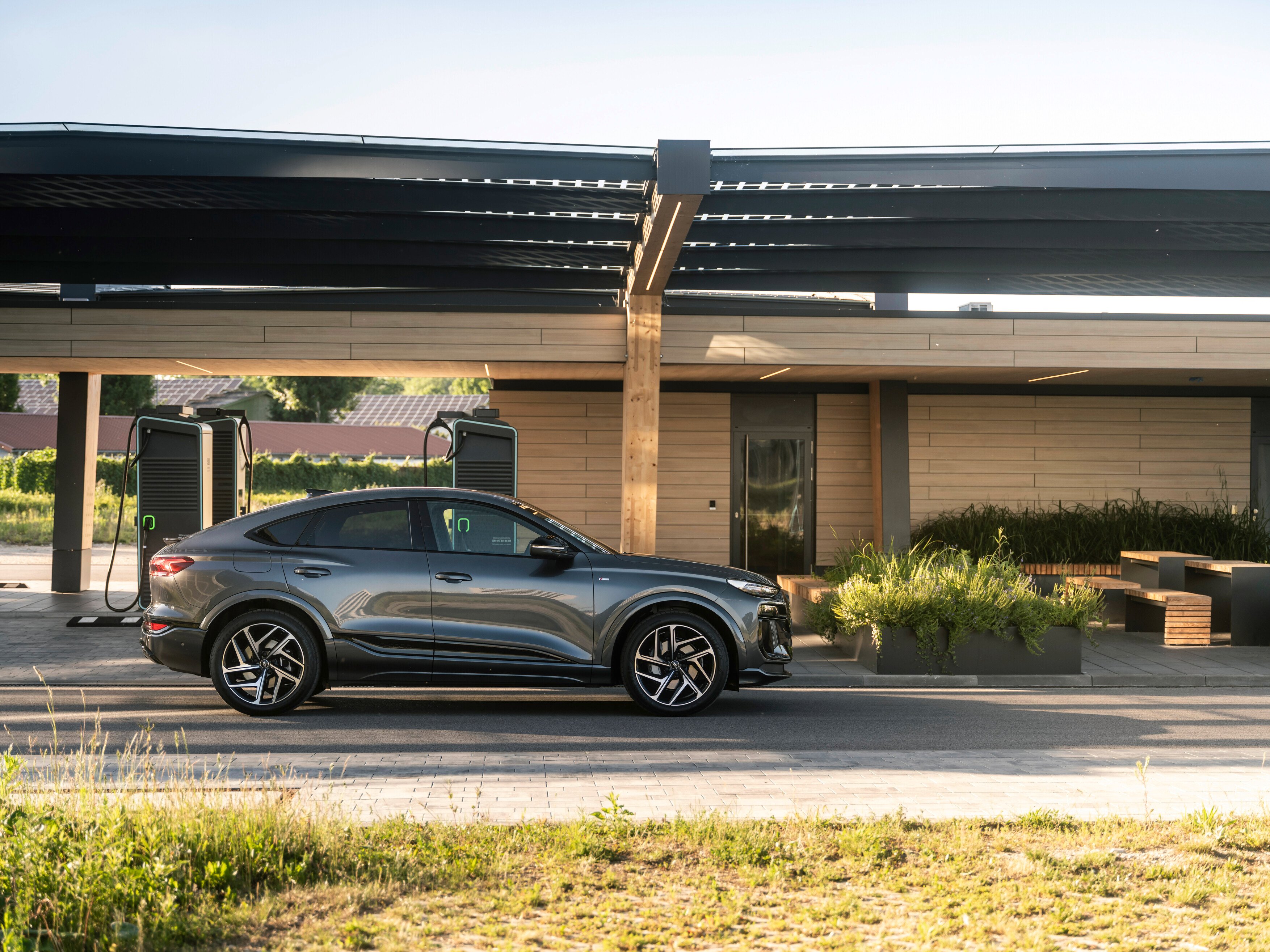 Siv Audi Q6 Sportback e-tron, parkiran ob sodobni električni polnilnici.