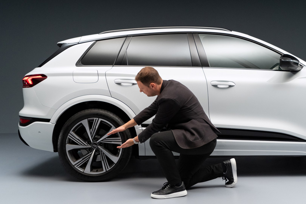 Andreas Ruf, vodja sistemske ekipe pri znamki Audi, kleči ob zadnjem desnem kolesu modela Audi SQ6 SUV e-tron z iztegnjenima rokama. 