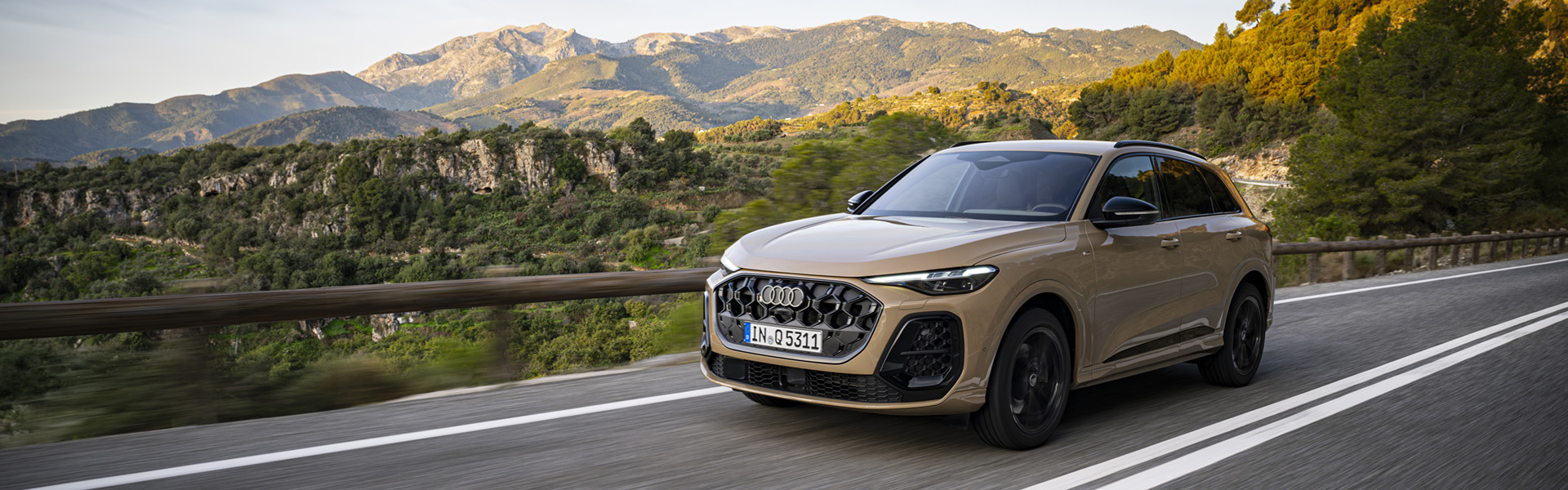 Audi Q5 na gorski cesti, v ozadju zeleni hribi v topli zlati svetlobi.