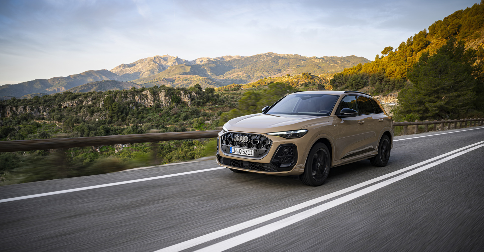 Audi Q5 na gorski cesti, v ozadju zeleni hribi v topli zlati svetlobi.