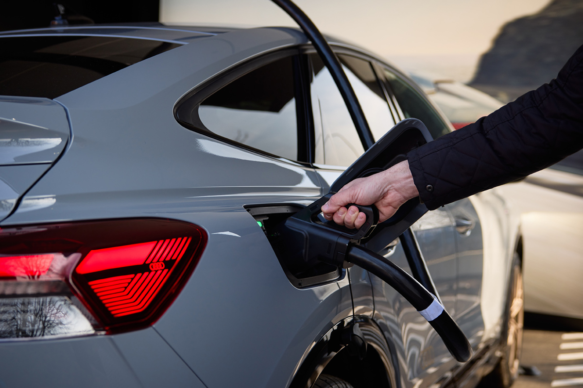 Roka priklaplja polnilni kabel na električno vozilo Audi, prikazano od zadaj z desne strani.