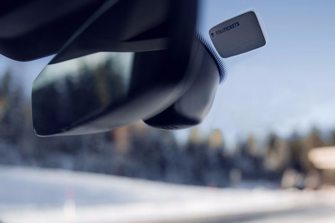Naprava Tolltickets na vetrobranskem steklu Audija, v ozadju zasnežena pokrajina in cestninska postaja.