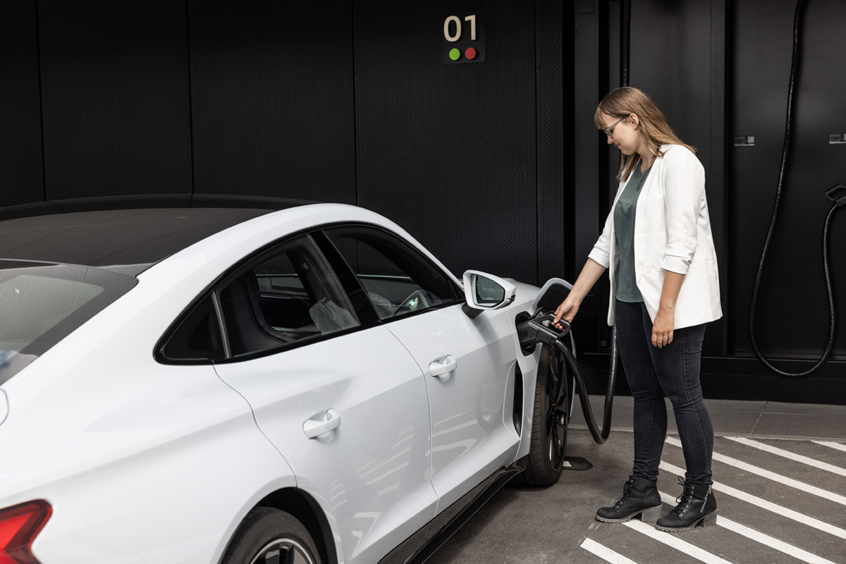 Oseba priklaplja polnilni kabel na belo električno vozilo Audi.