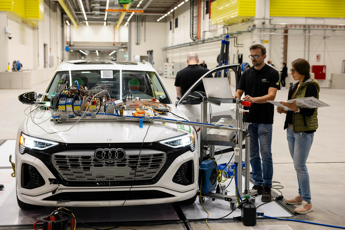 Bel Audi z merilno opremo na pokrovu. Dva inženirja pregledujeta podatke.