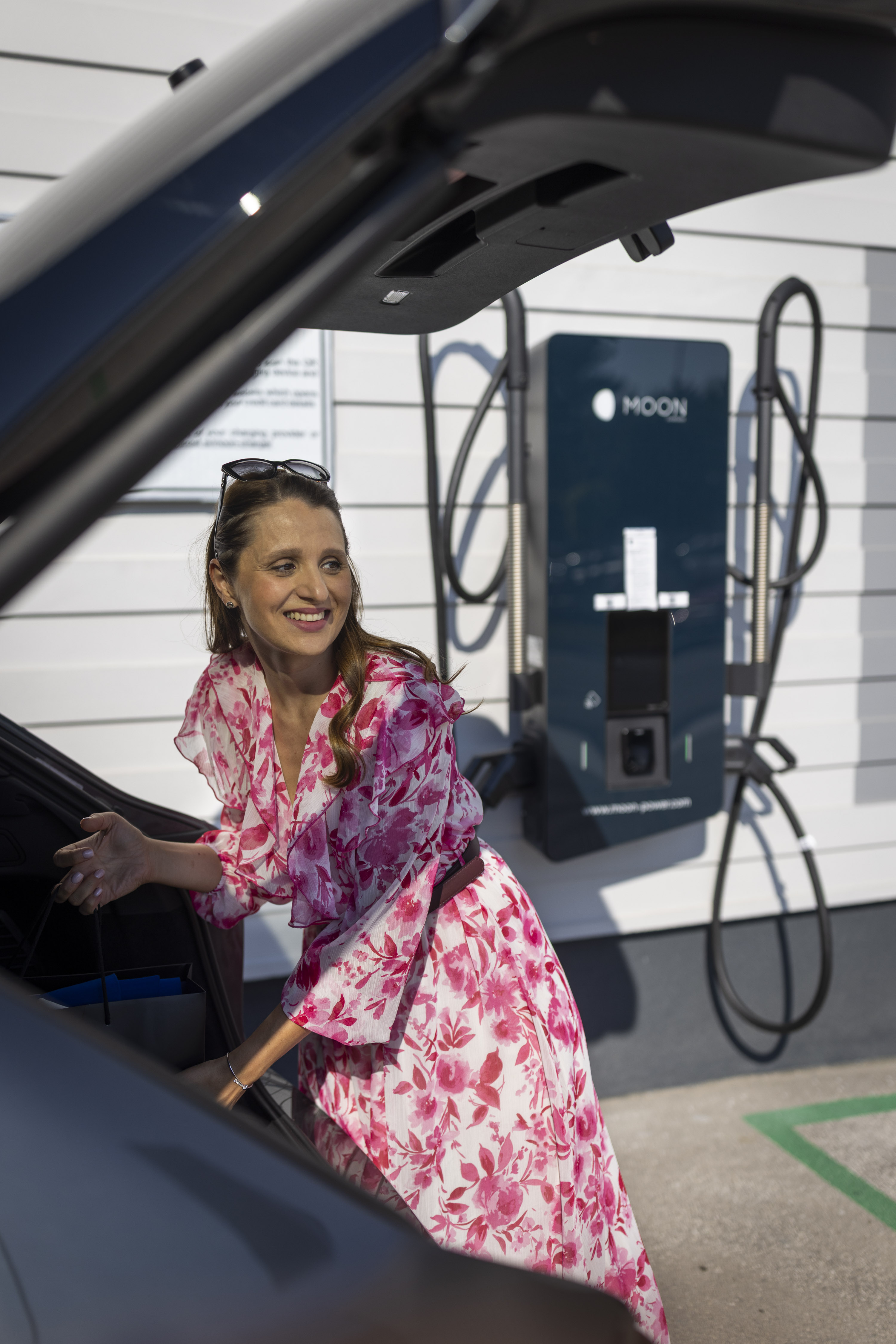 Mirela Ženska se nasmejano pripravlja na polnjenje električnega Audija Q6 e-tron pri polnilni postaji.